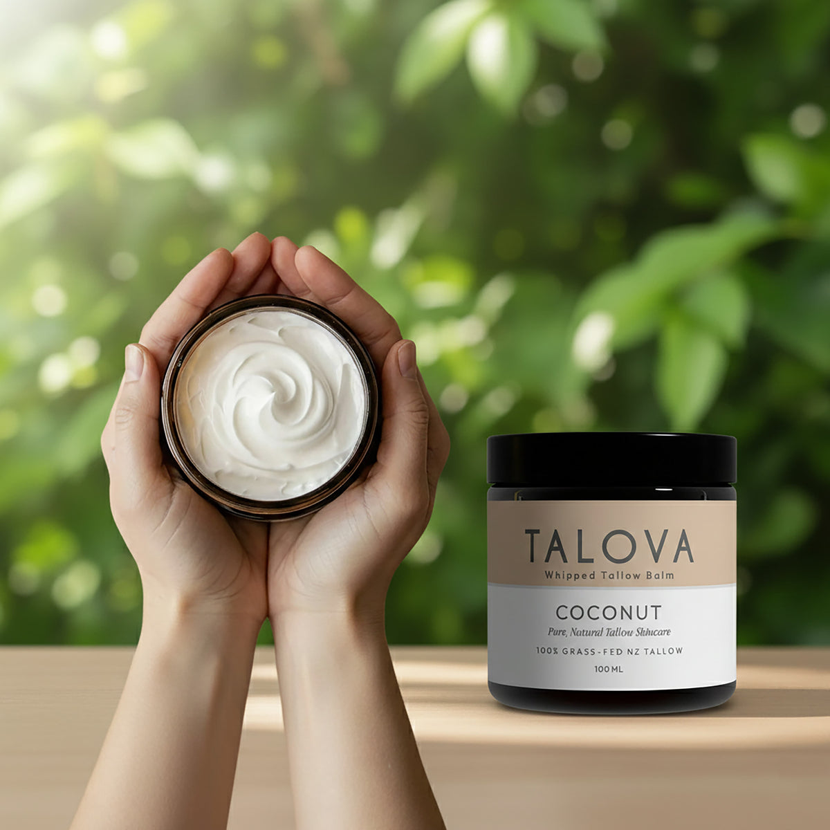 Talova coconut whipped tallow balm 100ml in hands cupping open jar with greenery background